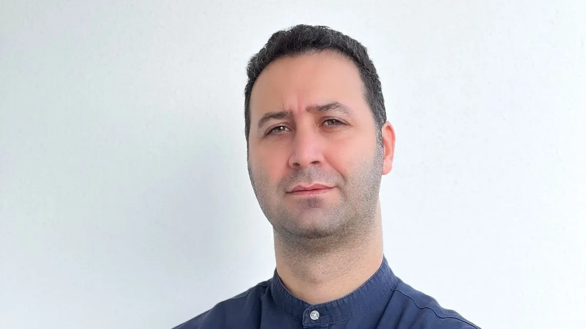 Koray Yalçın, beyaz duvar önünde lacivert gömlekle